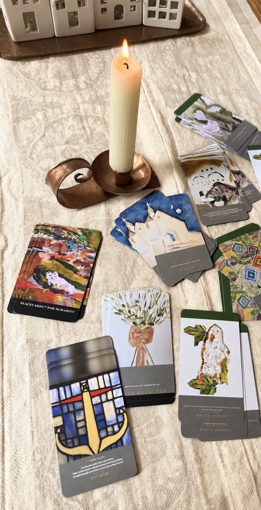 Peace Cards spread by candlelight on a linen tablecloth, showing the Cross, Anchor, Olive Branches and White Parrot cards
