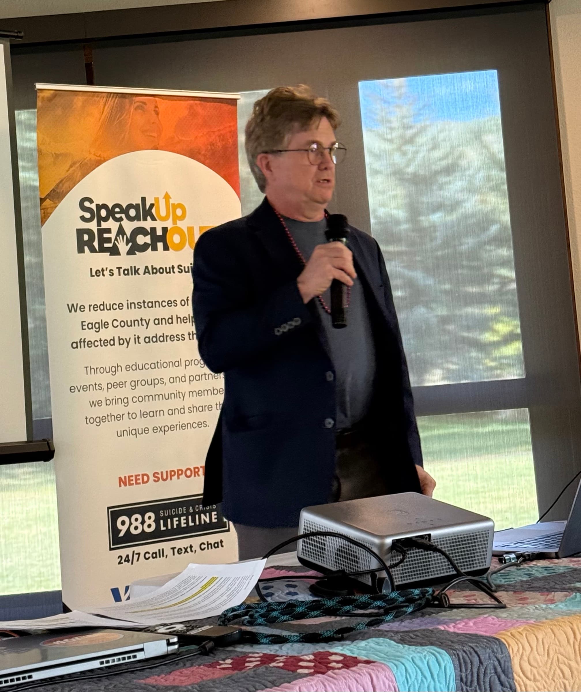 Jeff Jackson speaking into a microphone beside a SpeakUp ReachOut banner