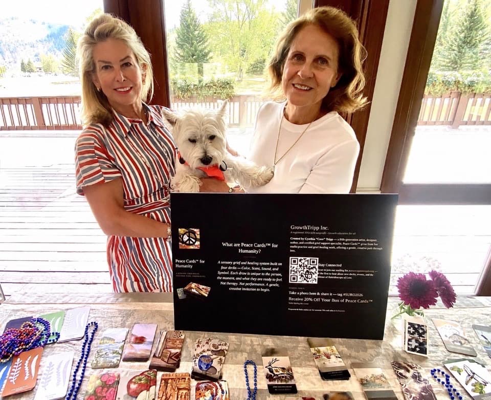 Cynthia Tripp and Jill Welsh holding Ollie behind the Peace Cards display table at the launch